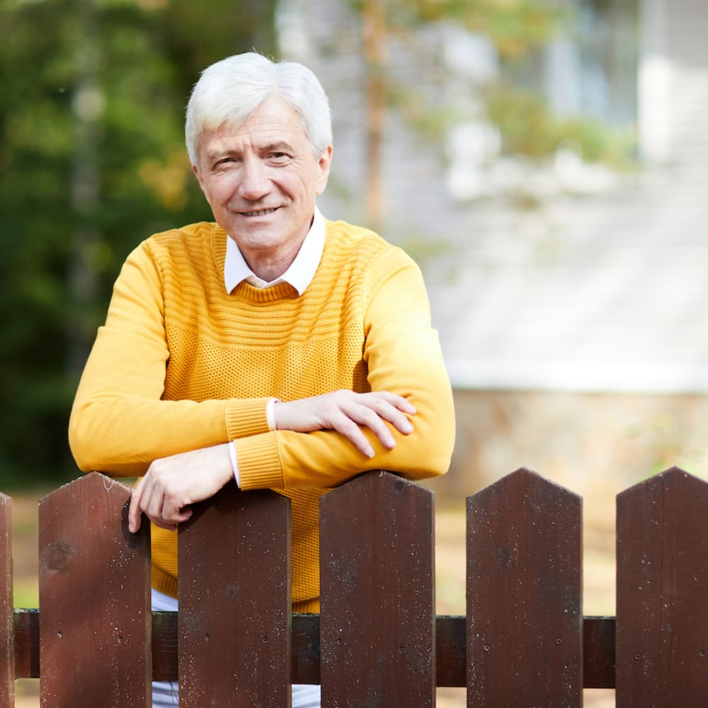 Senior man with grey hair leaning against wooden fence while looking at camera